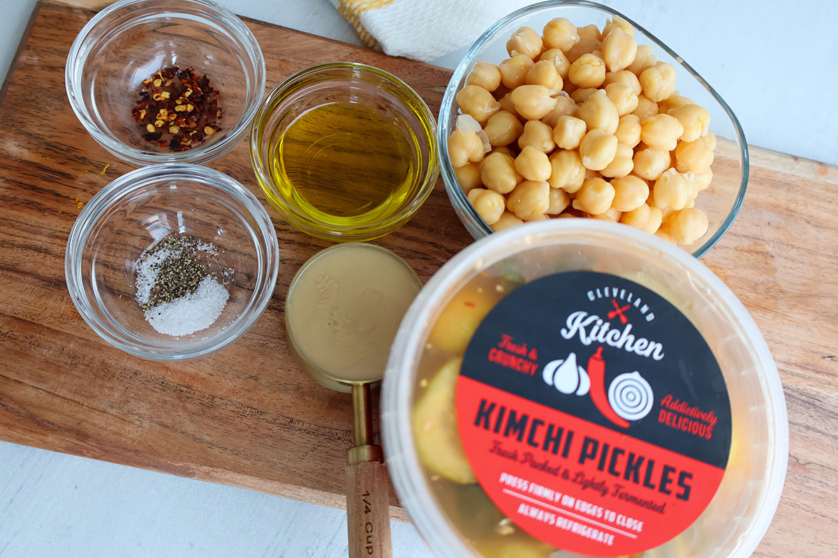 Individual pickle hummus ingredients on wooden board.