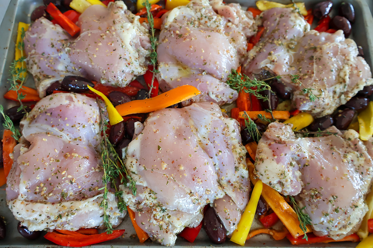 Unbaked chicken thighs and vegetables on a sheet pan