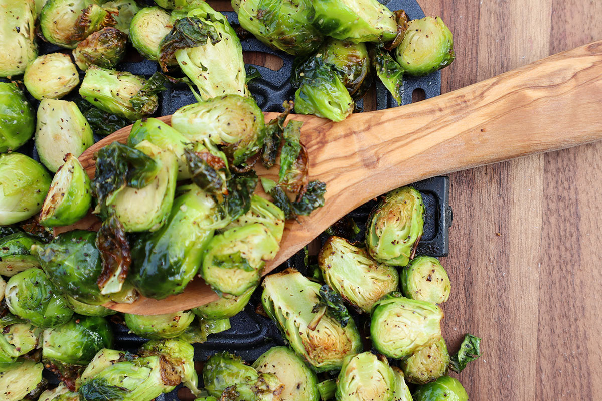 An overhead closeup shot of a wooden spoon scooping up air fryer brussel sprouts.