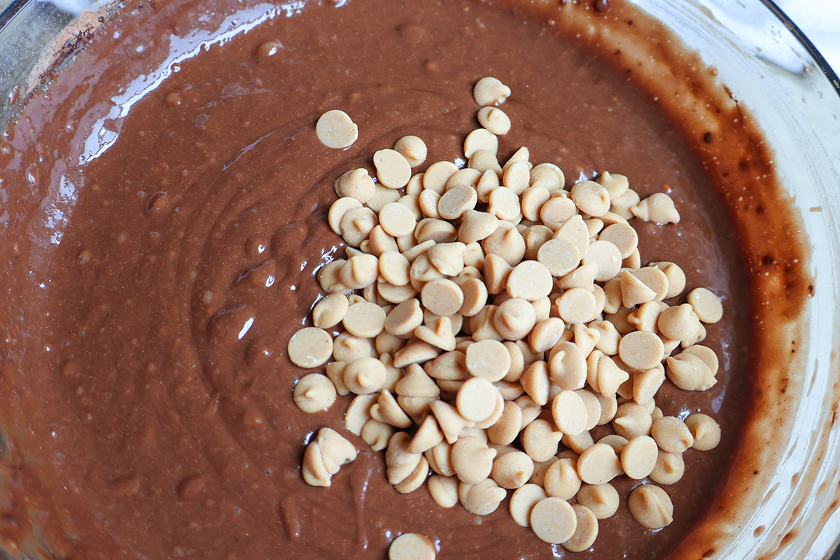Chocolate muffin batter with peanut butter chips in a mixing bowl.