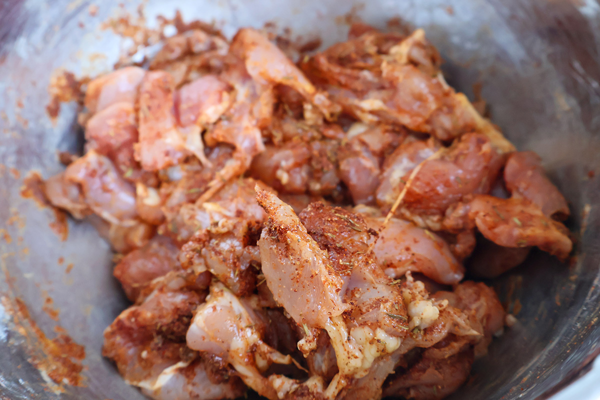 A metal bowl filled with seasoned raw chicken chunks.