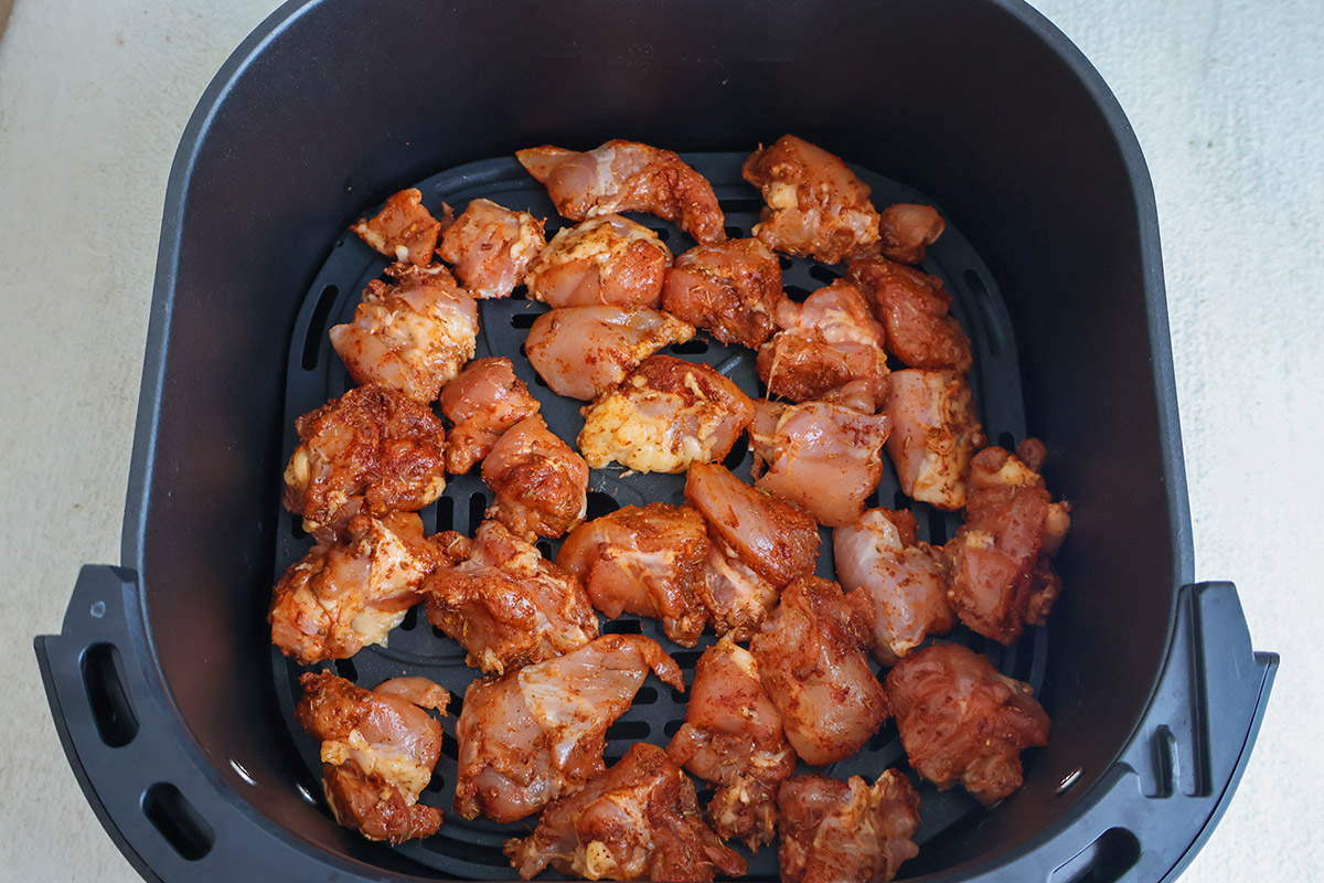 Raw seasoned chicken chunks in an air fryer basket.