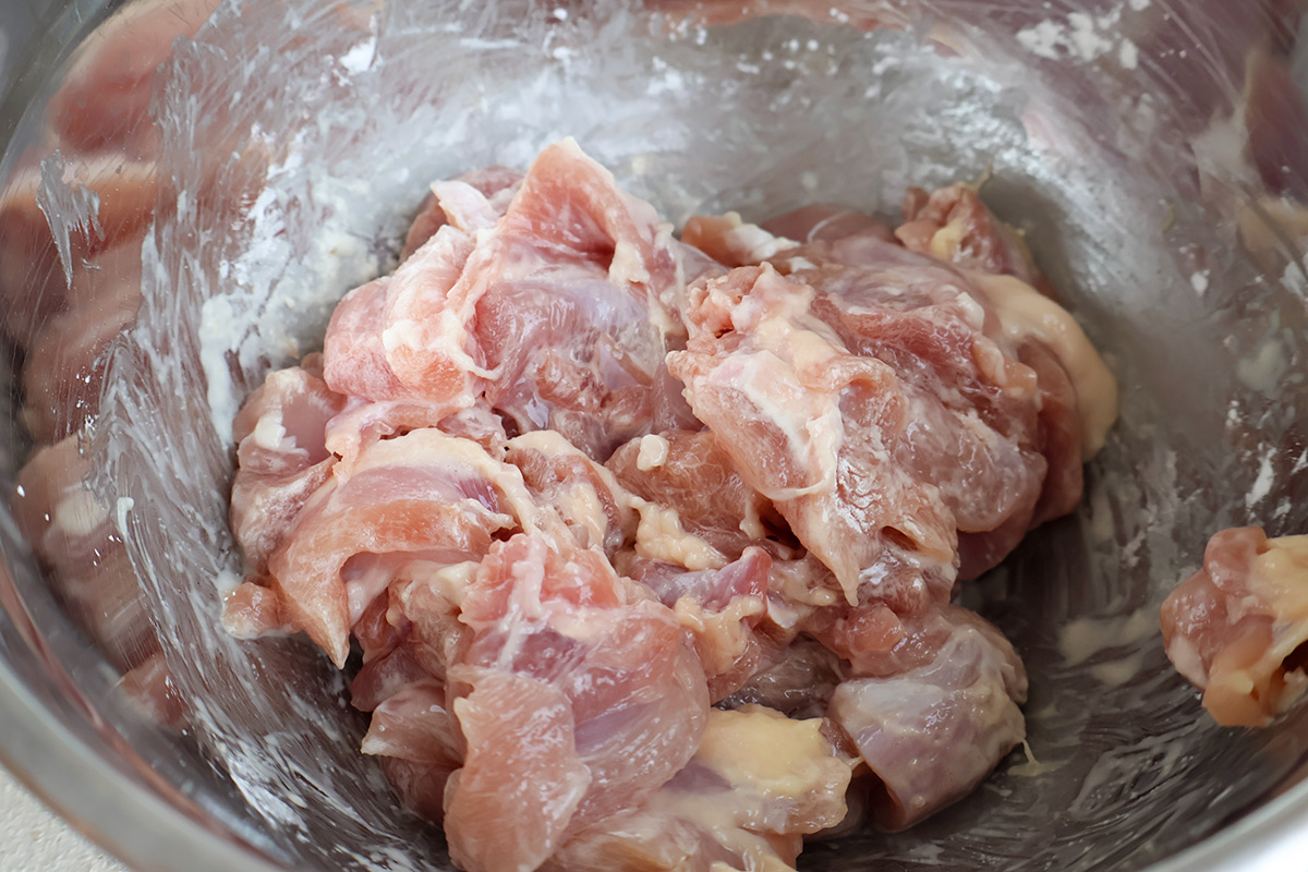 Raw chicken cubes mixed with cornstarch in a bowl.