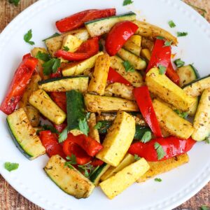 A mix of zucchini, squash, and bell peppers on a white plate.
