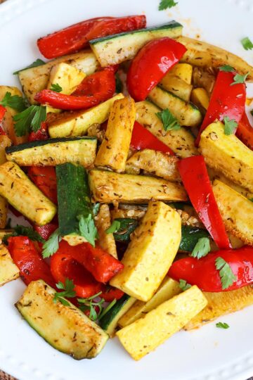 A mix of zucchini, squash, and bell peppers on a white plate.