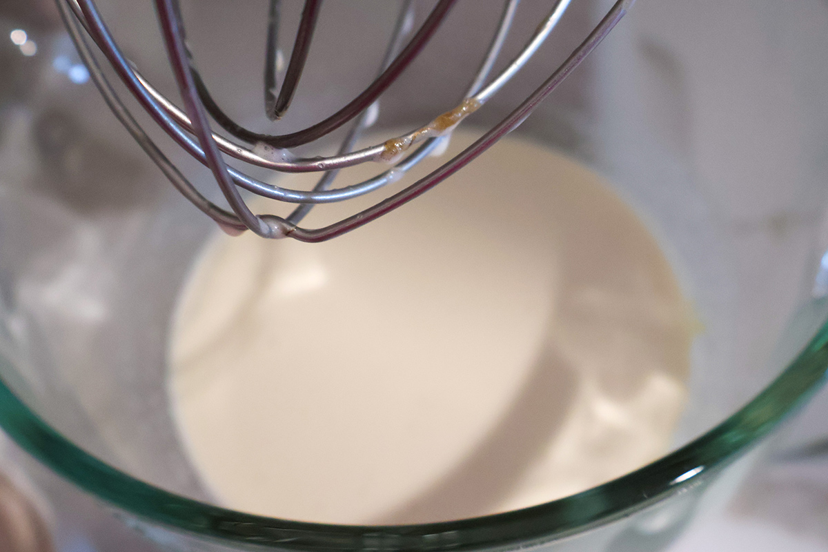 A whisk attachment over a glass bowl with wet muffin ingredients.