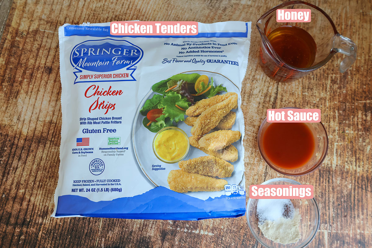 A bag of frozen chicken tenders with bowls of honey, hot sauce, and seasonings.