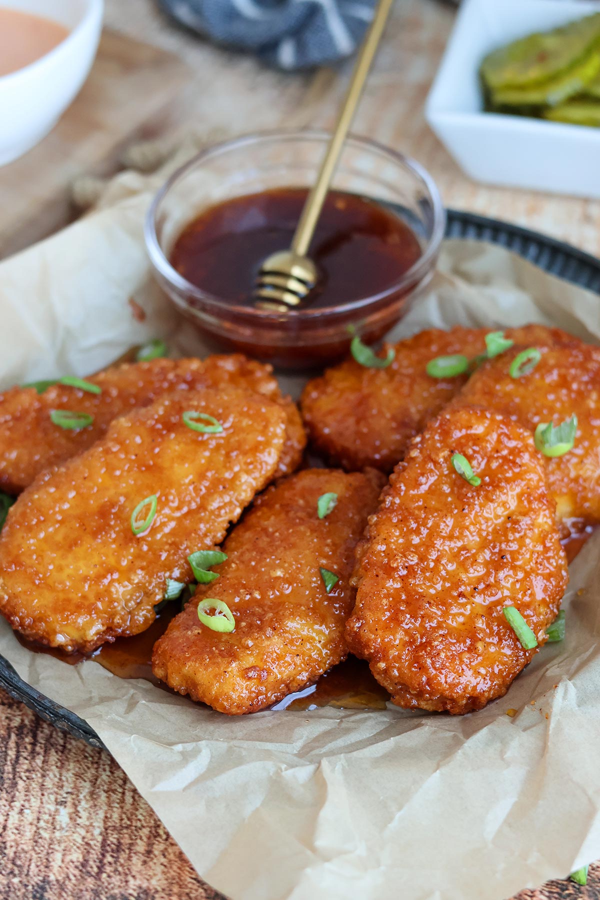 A plateful of four hot honey-glazed chicken tenders with a bowl of hot honey.