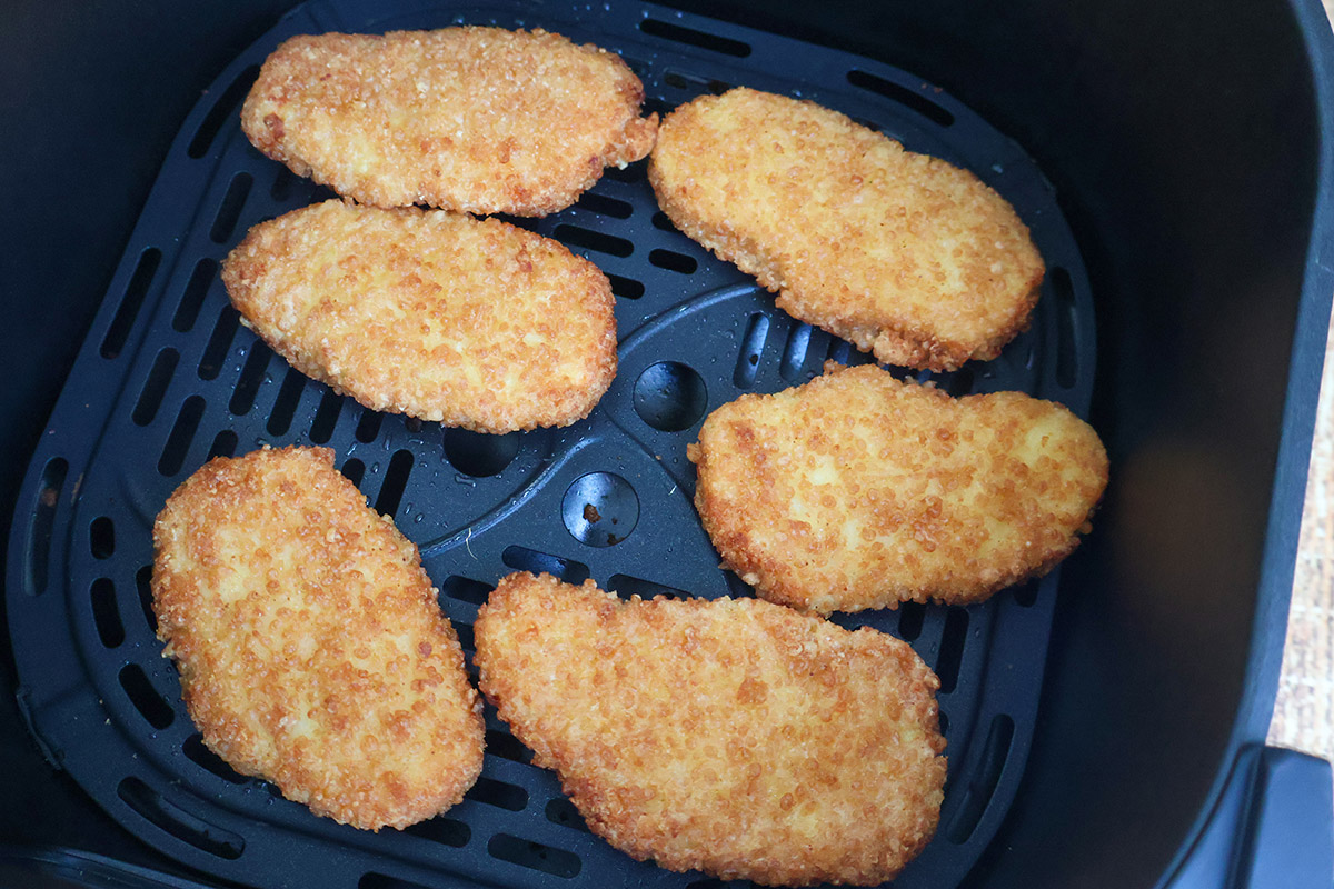 Six golden air-fried chicken tenders in an air fryer basket.