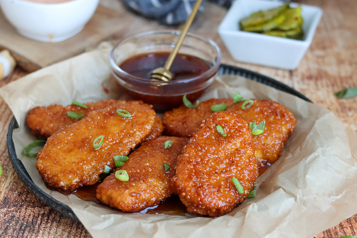 Five chicken tenders and a small bowl of honey on a plate.