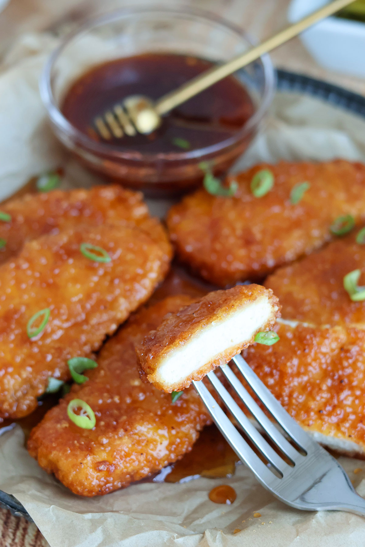 A fork with a piece of crispy chicken over a plate with five chicken tenders.