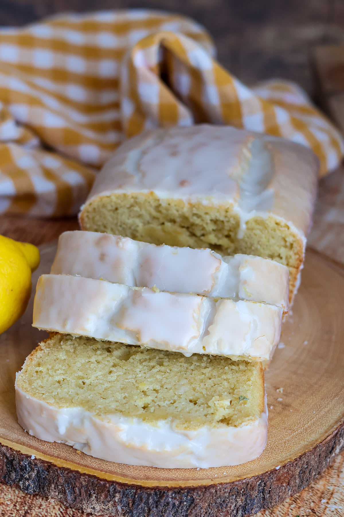 A sliced frosted lemon loaf cake on a wooden board.