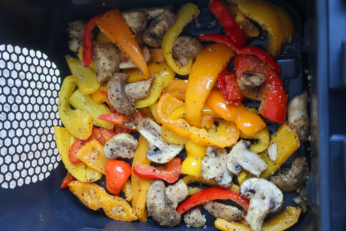 Cooked bell peppers and mushrooms in an air fryer basket.