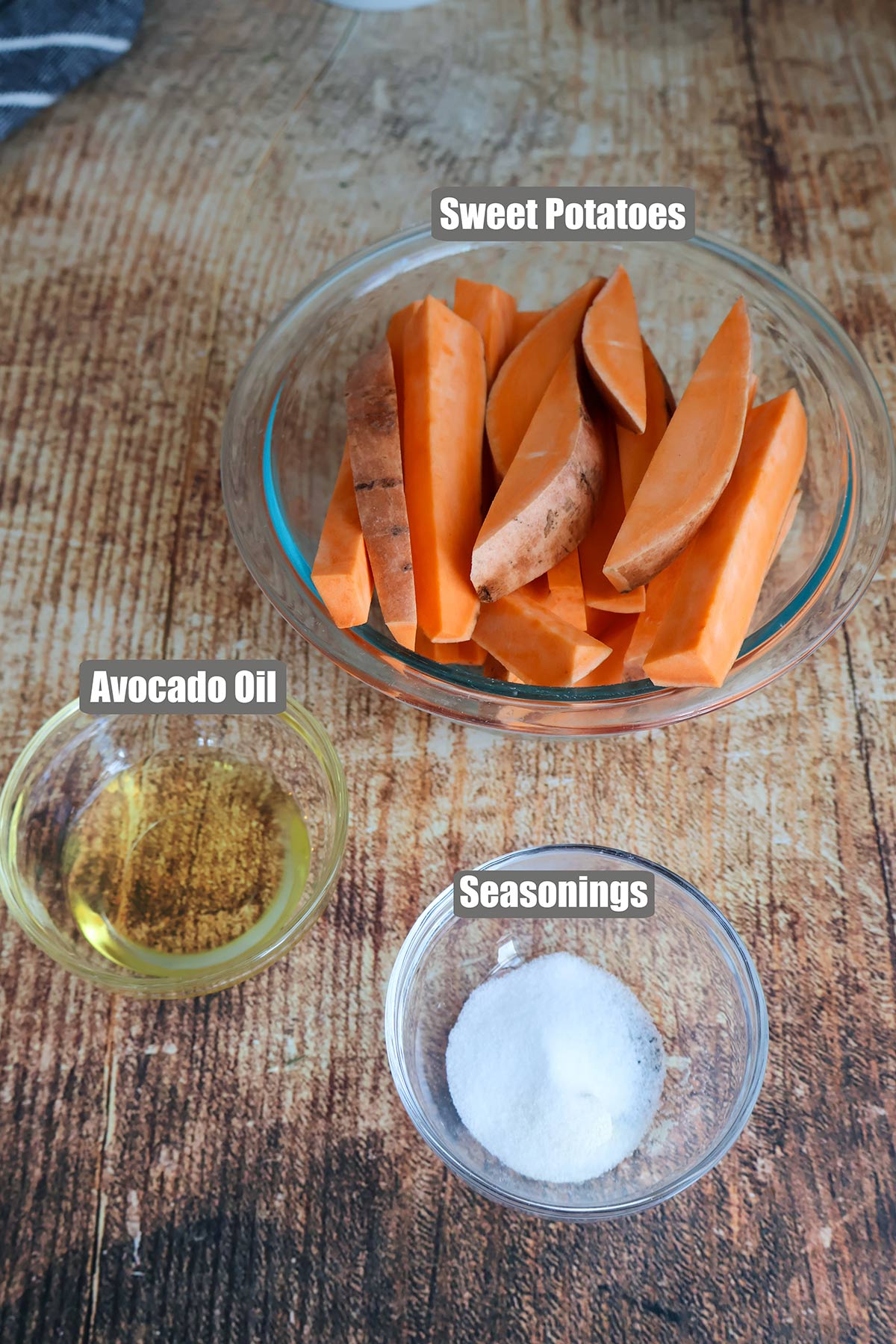Sweet potato wedges, oil, and seasonings in glass bowls.