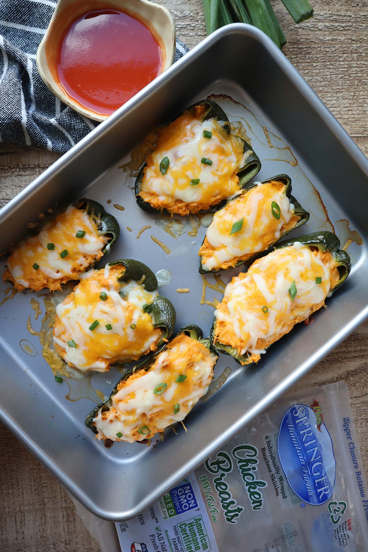 Six baked stuffed poblanos topped with cheese in a baking pan.