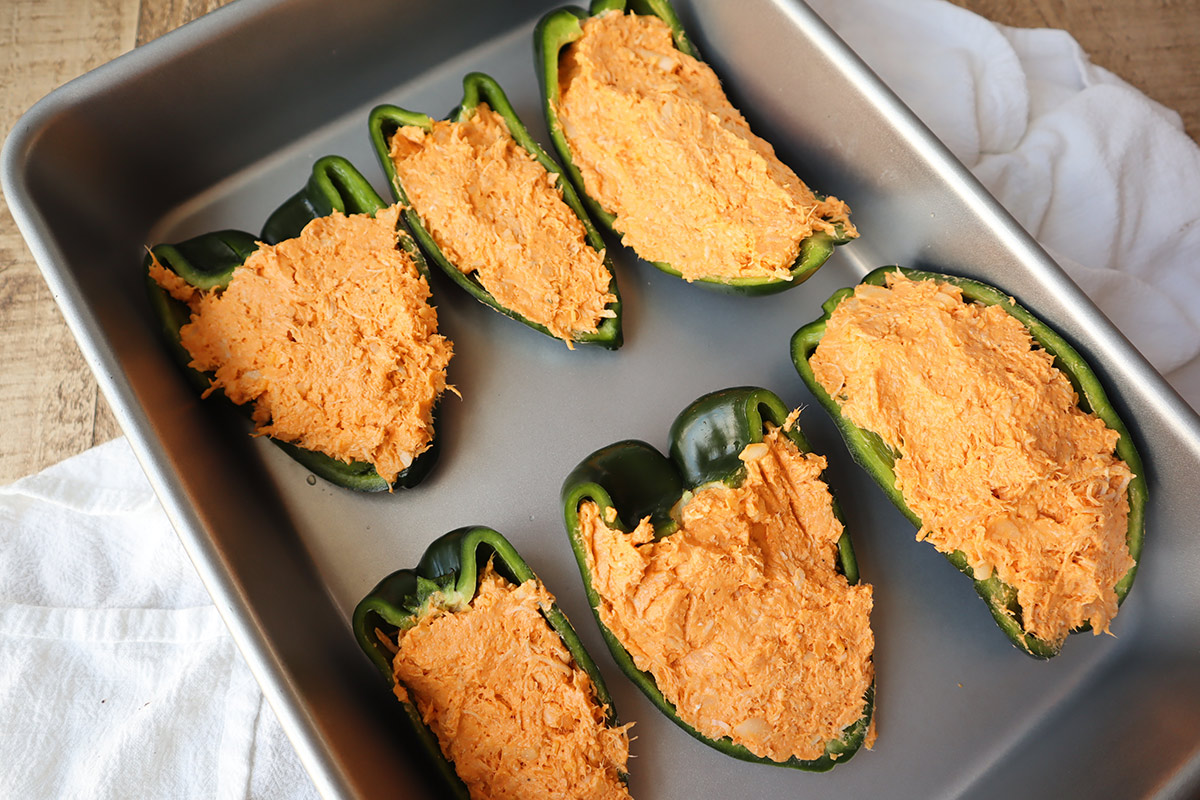 Six unbaked poblano peppers stuffed with chicken mixture in a baking pan.