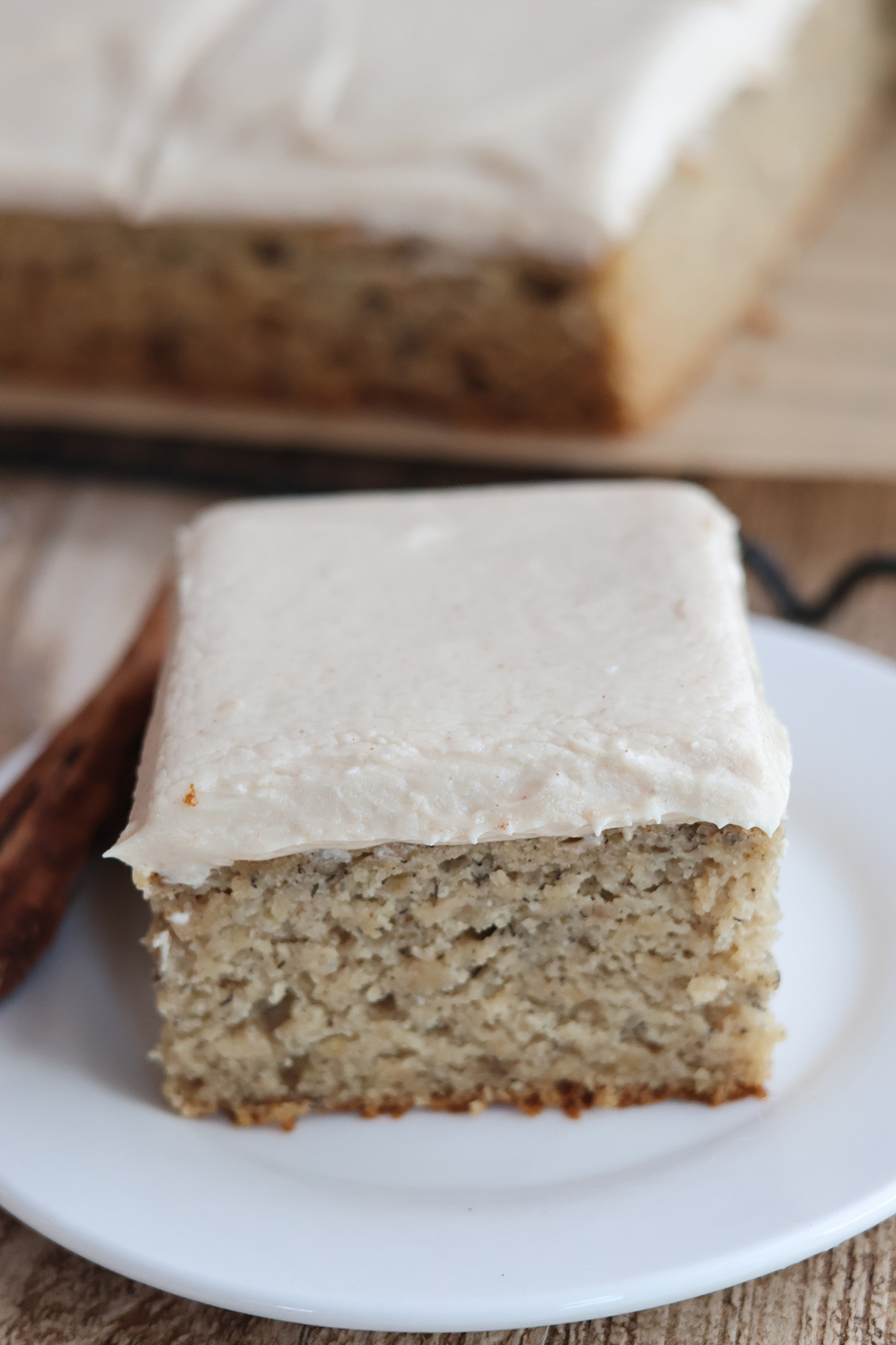 A slice of frosted banana cake on a white plate. 