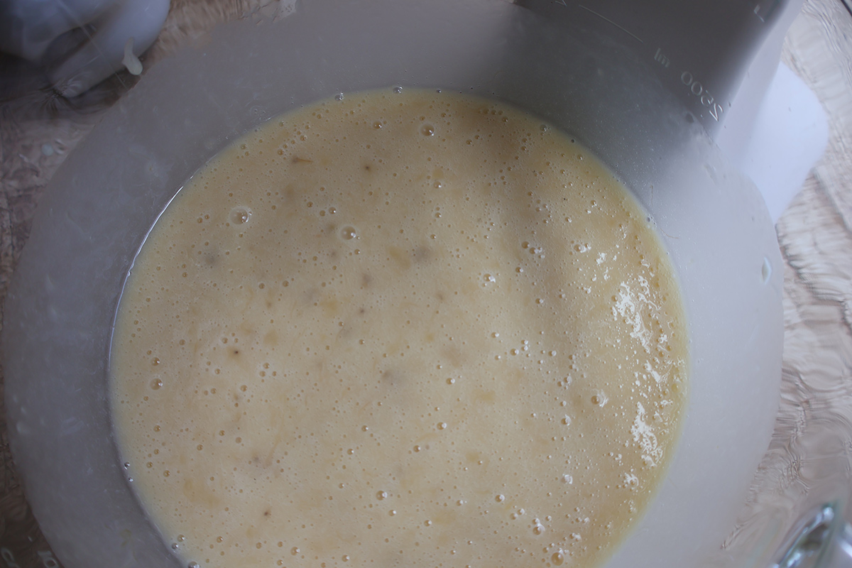 A glass mixing bowl with wet banana cake ingredients. 