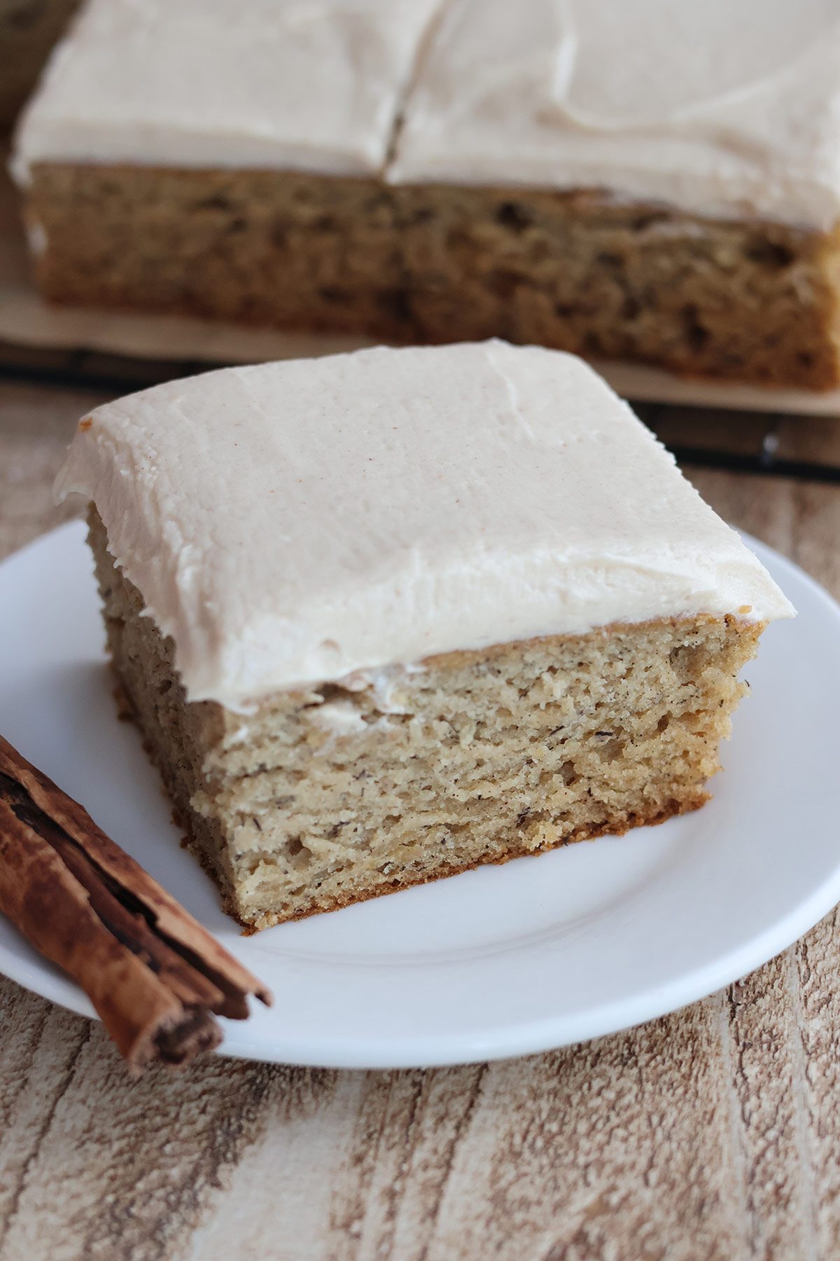Slice of frosted banana cake on a white plate.