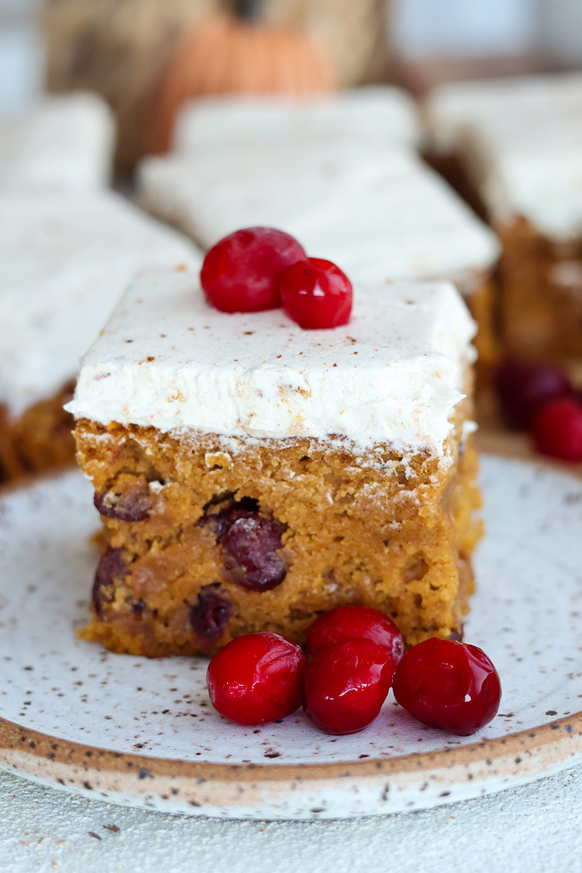 A slice of frosted pumpkin cake with three cranberries on a plate.
