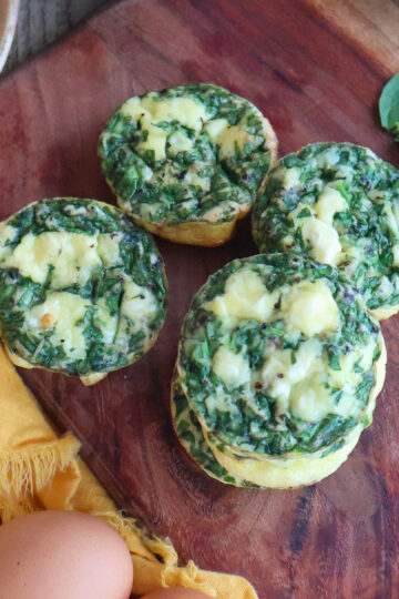 Four spinach and egg cups on a cutting board.