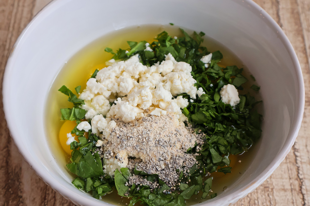 A mixing bowl filled with eggs, spinach, and feta.