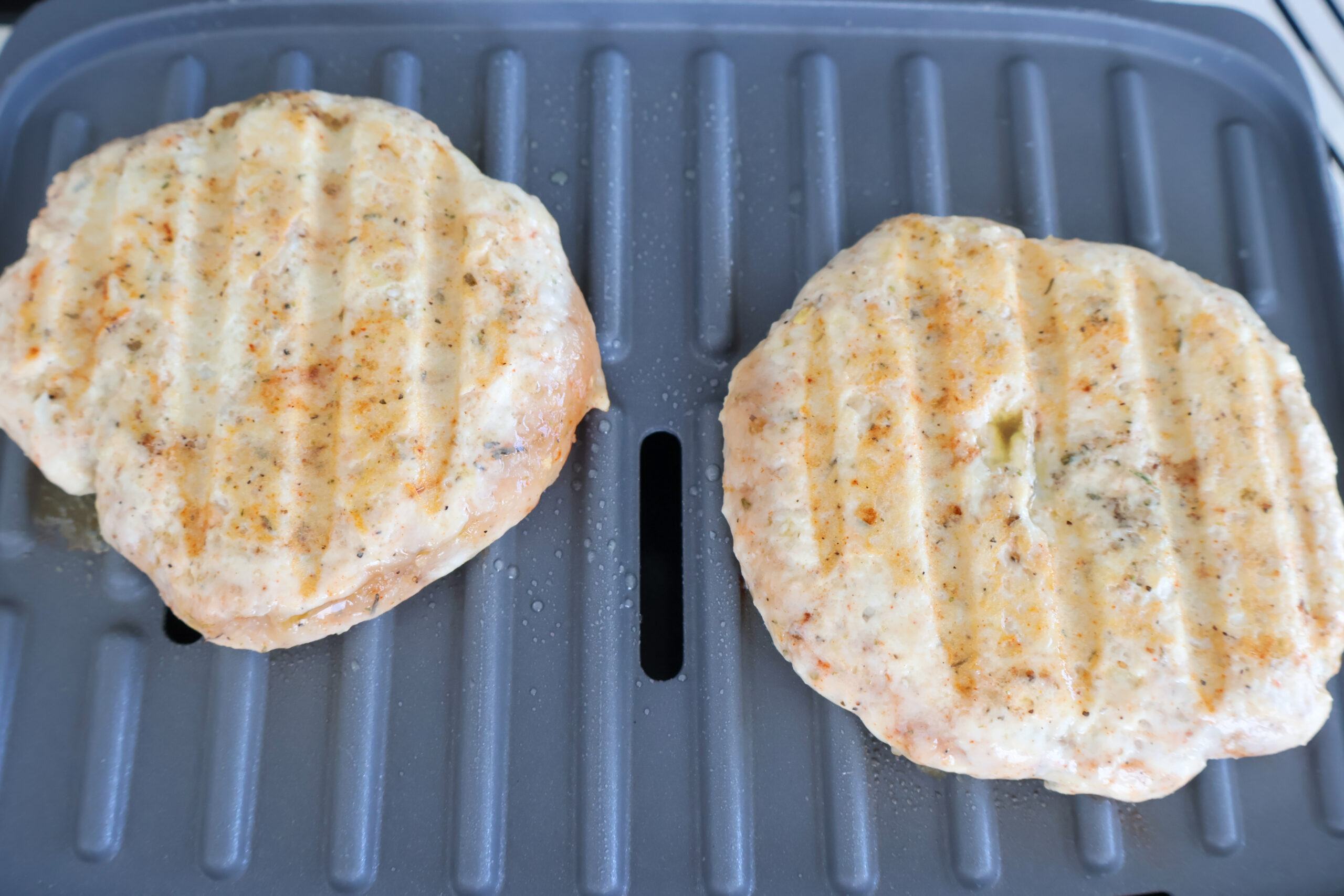Raw grilled chicken patties on a grill plate.
