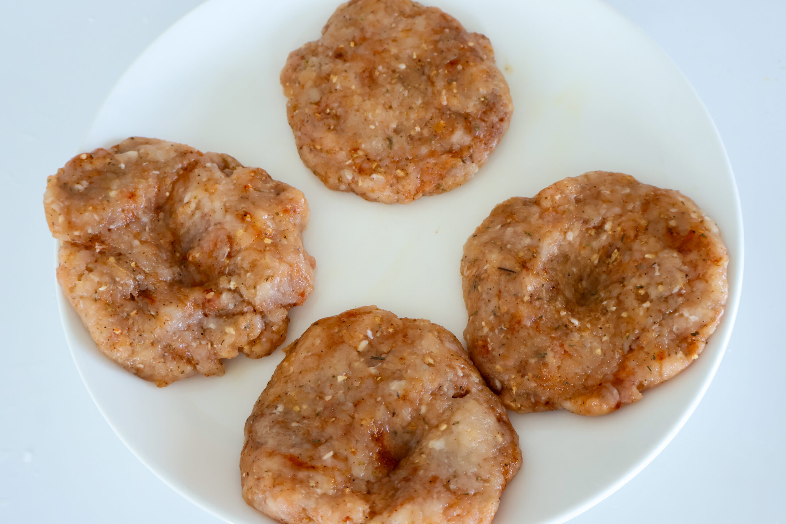 Ground chicken burger patties on a white plate.