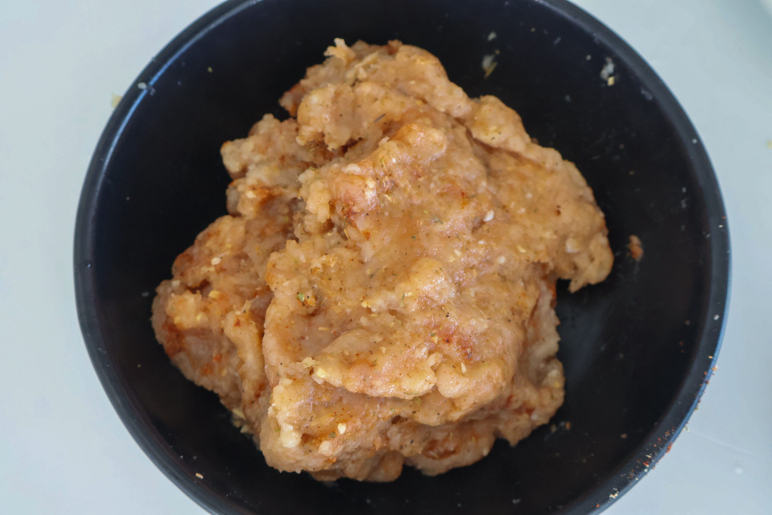 Ground chicken burger mix in a black bowl.