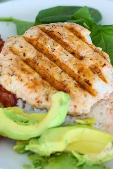 A chicken burger with avocado and bacon on a plate of rice.