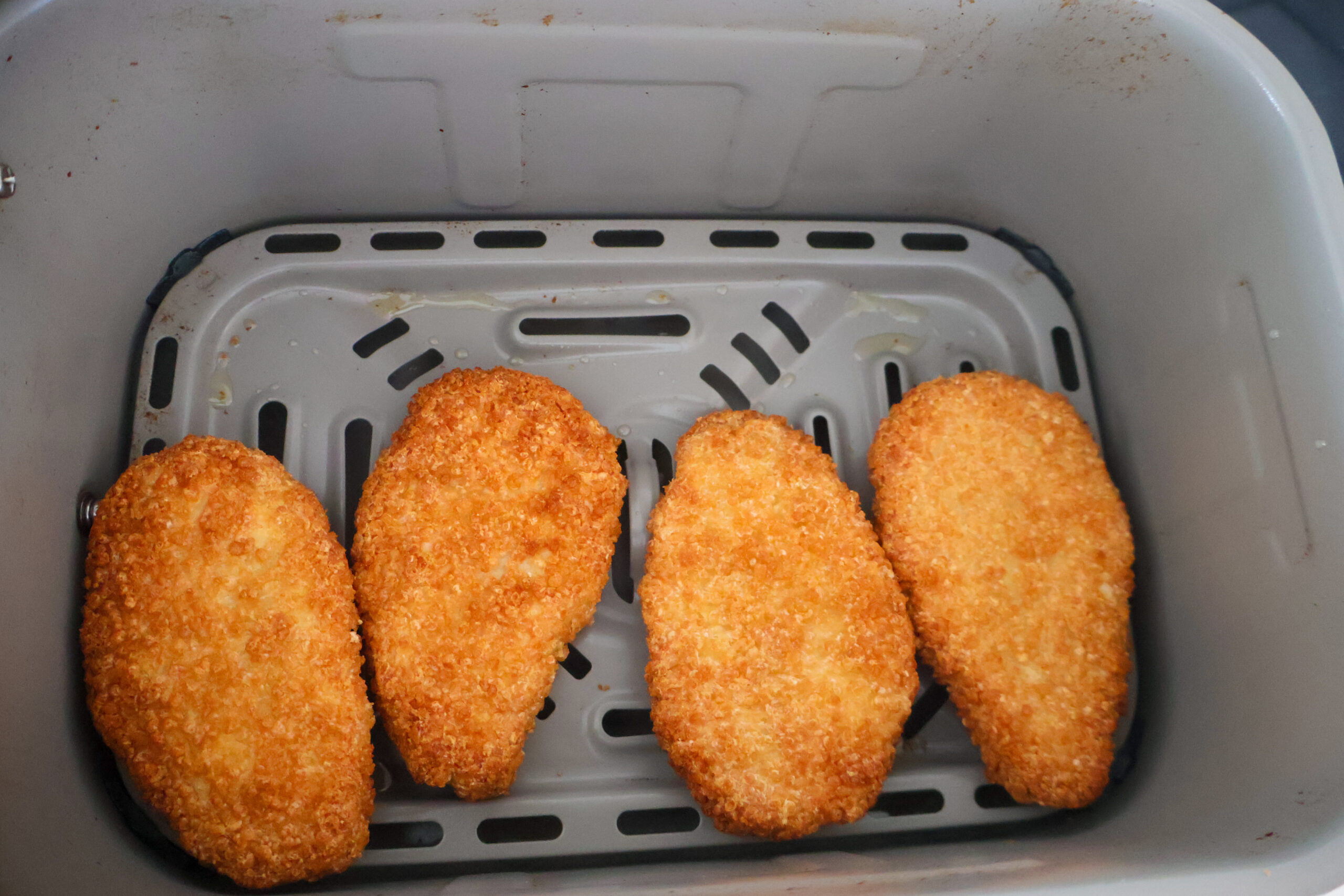 4 chicken strips in an air fryer tray.