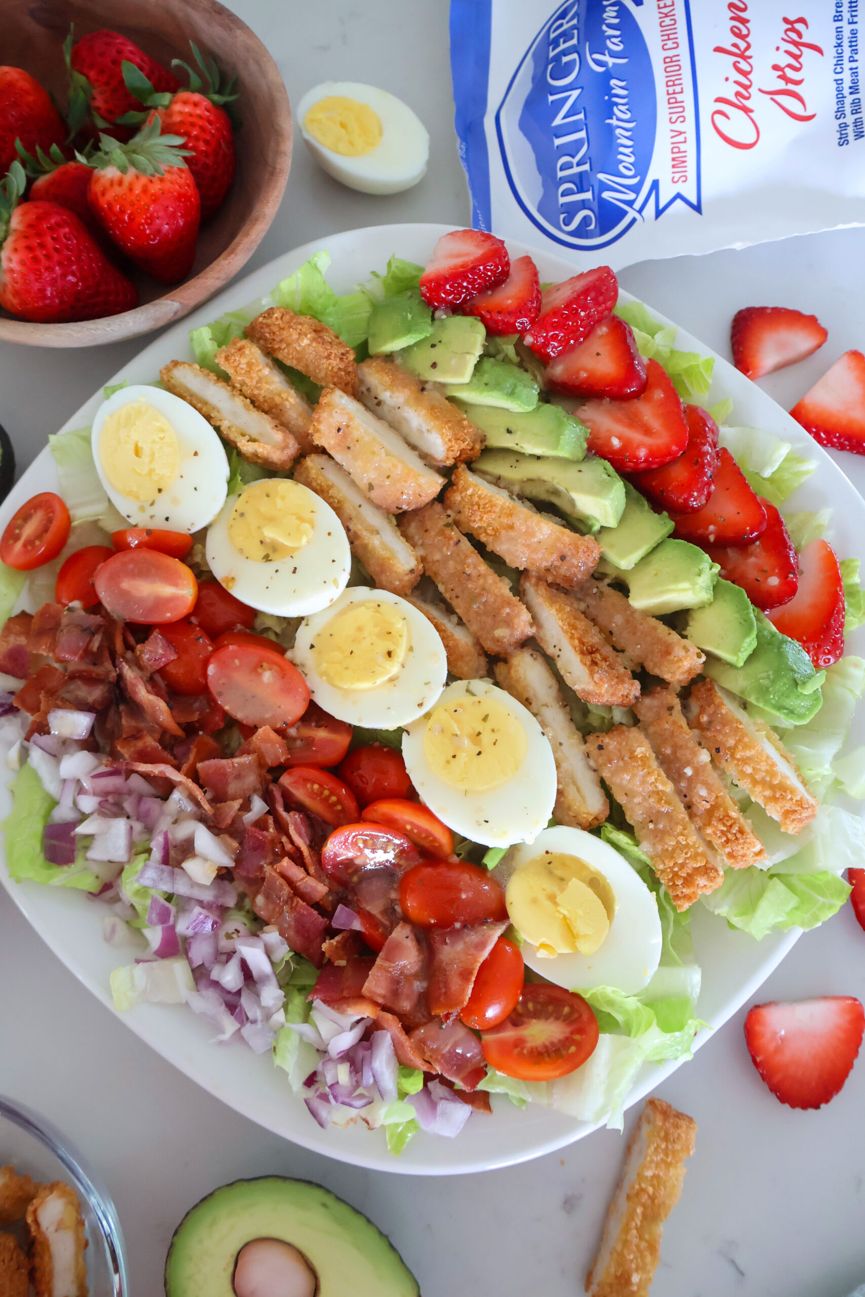 A large plate of strawberry cobb salad with eggs and avocados on the side.