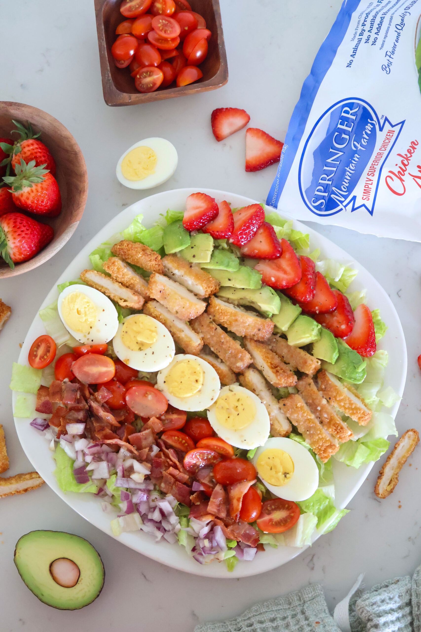 A large plate of strawberry cobb salad with strawberries on the side.
